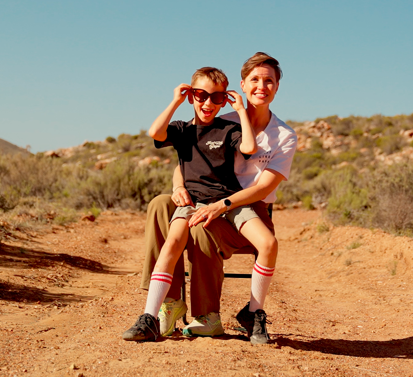 A smiling boy sitting on his moms lap in a rough terrain